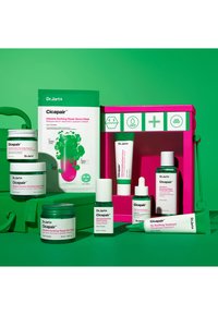 Cicapair hudpleieprodukter med grønn og hvit emballasje på en lys grønn bakgrunn. Inkluderer krukker, tuber og en rosa beholder.