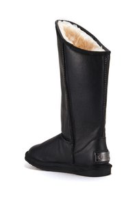 Czarny skórzany but z wysoką cholewką, miękkim beżowym futrem wewnątrz oraz płaską gumową podeszwą. Posiada przeszycia oraz metalową metkę logo z tyłu.