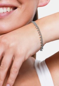 Bracciale in argento con piccoli accenti sferici lungo una delicata catena, indossato su un polso chiaro. Texture liscia e lucida.