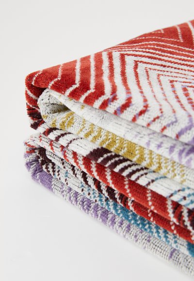 Stapels textuurhanddoeken in rood, wit, geel, paars en blauw. Elke handdoek heeft verschillende geometrische patronen en variërende kleuren.