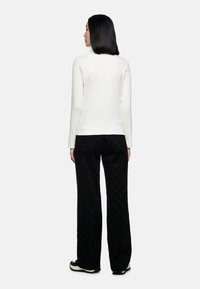 Langärmliges weißes Oberteil kombiniert mit einer schwarzen Cordhose mit einem subtilen Sternmuster, abgerundet mit schwarzen Schuhen mit weißen Sohlen.