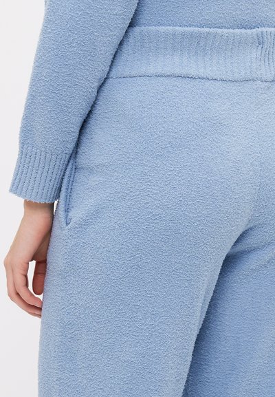 Fatos de treino azul claro em fleece com punhos canelados, bolsos laterais e uma superfície macia e texturizada. Cintura elástica para maior conforto.