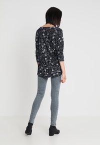 Tunic nera a fiori con maniche a tre quarti, caratterizzata da motivi floreali bianchi. Abbinata a jeans skinny grigi chiari e stivali neri alla caviglia.
