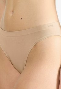 Beige Unterwäsche mit glatter Textur, ausgestattet mit einem breiten Bund und dezentem Logo-Branding. Das Design ist minimalistisch und nahtlos.