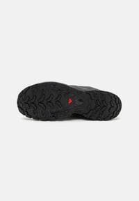 Black rubber sole featuring a rugged tread pattern with raised accents, including a red triangular emblem at the center for traction.