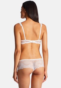 Ensemble de lingerie en dentelle blanche avec un motif floral délicat, des bretelles réglables et une fermeture à crochets au dos. Texture douce et transparente.