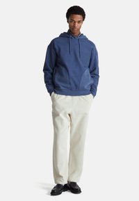 Marineblauwe hoodie met een gestructureerde afwerking, capuchon met trekkoord en grote kangoeroezak, gecombineerd met lichtcrème corduroybroek en zwarte schoenen.