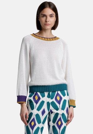 White knitted sweater with multicolored ribbed collar and cuffs. Paired with patterned pants featuring large teal and purple diamonds.