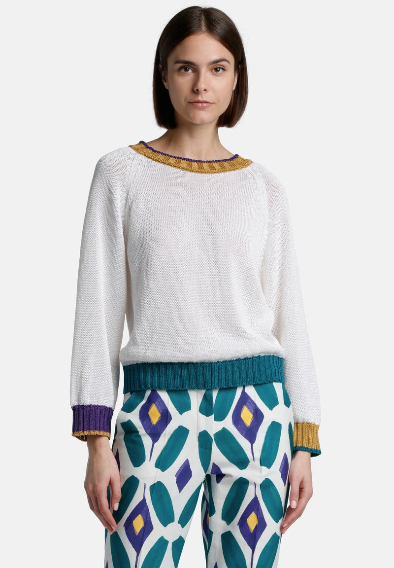 White knitted sweater with multicolored ribbed collar and cuffs. Paired with patterned pants featuring large teal and purple diamonds.