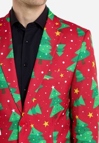 Rode kerstblazer met groene kerstbomen, gele sterren en witte stippen; gemaakt van stof met een gladde textuur en twee knopen.