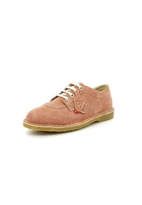 Chaussure en suede beige avec un bout arrondi, des lacets blancs et des détails de couture. Elle dispose d'une semelle en caoutchouc et d'une étiquette attachée près des lacets.