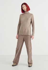 Bruine coltrui met een zachte textuur, gecombineerd met ruime bruine corduroy broeken. Casual pasvorm en slanke silhoutte.