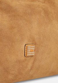 Sac en daim beige avec un accent métallique carré orné de clous circulaires. Texture douce avec un design minimaliste.