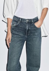 Džínové kalhoty v tmavě modré barvě, s rovnými nohavicemi, pěti kapsami, zipem s knoflíkovým zapínáním a jemným vyblednutím na látce.