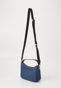 Blue fabric crossbody bag with a curved zipper top, black leather accents, and an adjustable black strap. Textured surface. Compact shape.
