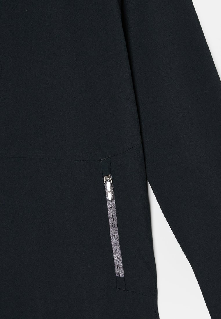 Nahaufnahme des Ärmels einer schwarzen Jacke mit einer senkrechten Reißverschlusstasche, die einen silbernen Reißverschlussgriff und grauen Reißverschlussstoff zeigt.