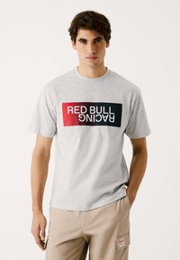 Pelēka kokvilnas t-krekls ar taisnstūra "Red Bull Racing" logotipu melnā un sarkanā ombre krāsā. Apaļa kakla izgriezums, īsas piedurknes, brīva piegriezuma.