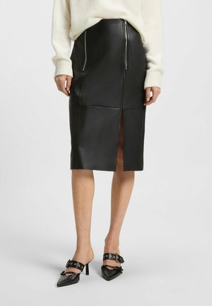 Gonna a matita in pelle nera con uno spacco frontale, caratterizzata da dettagli con zip e accenti di cucitura. Indossata con tacchi alti neri appuntiti dal design con cinturini.