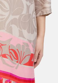 Sukienka w kwiatowy wzór w jasnym beżu, różu i czerwieni. Posiada zwiewny materiał o miękkiej fakturze oraz krótkie rękawy, podkreślające wyraziste kolory.