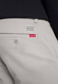 Grå Levi's-byxor med en etikett som visar "LEVI STRAUSS CALIFORNIA" och en röd Levi's-logga, som framhäver ett slätt tyg och knapppdetalj.
