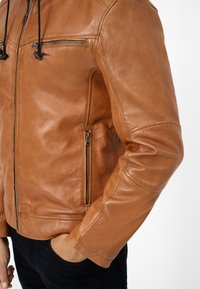 Helle Lederjacke mit einem Reißverschlusstasche auf der Brust und seitlichen Taschen, mit einer enganliegenden Passform und sichtbaren Nähdetails.