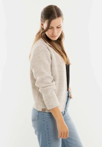 Lichtbeige gebreide cardigan met een ribbelstructuur, lange mouwen en een ontspannen pasvorm, gecombineerd met lichtblauwe spijkerbroek.