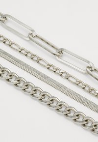 Sidabriniai metaliniai grandinukai įvairių dizainų ir tekstūrų, įskaitant susijungimus, lygų gyvatės grandinę ir storesnę curb grandinę.