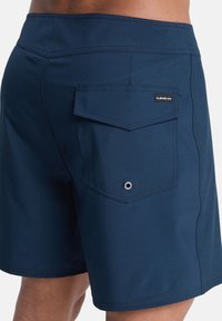 Ναυτικό μπλε μαγιό φτιαγμένο από ελαστικό ύφασμα, με πίσω τσέπη με κλείσιμο καπακιού και μικρή μεταλλική λεπτομέρεια ματιού.