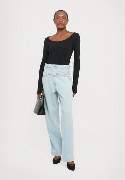 Maglietta nera a maniche lunghe con scollo a giro, abbinata a jeans a vita alta di colore blu chiaro e a gamba larga. Scarpe nere a punta e una borsa grigia.