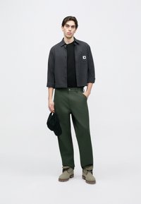 Γκρι πουκάμισο καρό, μαύρο t-shirt, παντελόνι χακί, γκρι μπότες και μαύρο καπέλο. Το πουκάμισο έχει λογότυπο σε σήμα και άνετη εφαρμογή.