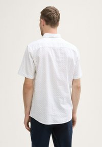 Chemise blanche à manches courtes, ajustée, avec un motif subtil de petits points bleus et un col boutonné. Texture en coton lisse.