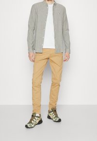 Ljusgrå knappad skjorta över en vit T-shirt, parat med tan chinos och gröna och svarta sneakers med gula accenter.