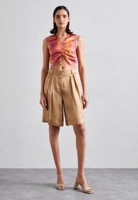 Kort, rosa og oransje tie-dye crop top med V-hals; beige plisserte shorts; lyse blokk-hæl sandaler. Jevne teksturer gjennomgående.