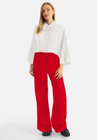 Witte, oversized blouse met een grote kraag; gecombineerd met felrode, losse broek. Zwarte schoenen maken de outfit compleet.