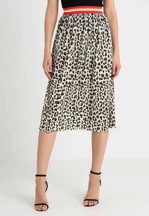 Femme portant une jupe midi plissée à imprimé léopard avec une ceinture rayée rouge, blanche et orange et des sandales à talons hauts noires.