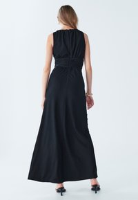 Vestido maxi negro con tejido texturizado, diseño sin mangas, escote fruncido y cintura ajustada que crea una silueta fluida.