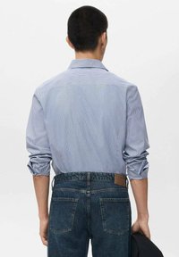 Blauw-wit gestreepte shirt met een klassieke kraag, opgerolde mouwen en een rechte snit, gedragen met donkere spijkerbroek. Achteraanzicht.