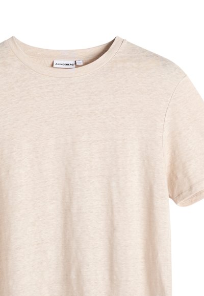 T-shirt beige à manches courtes et col rond avec une texture subtile et une étiquette de marque J.LINDEBERG à l'intérieur du col.