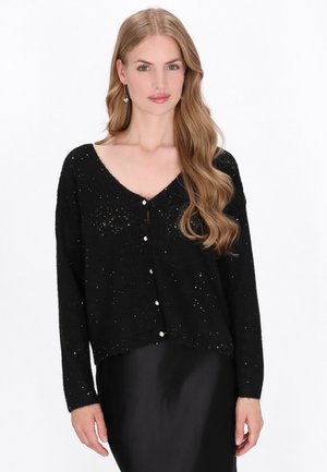 Cardigan nero lavorato a maglia con scollo a V, maniche lunghe e bottoni in perle. Il tessuto testurizzato presenta piccoli accenti scintillanti in tutto.