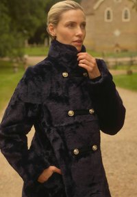 Tumši zils mākslīgās kažokādas mētelis ar augstu apkakli, divkāršu aizdari ar zelta toņa pogām un priekšējām kabatām. Mīksta tekstūra un silta izskata.