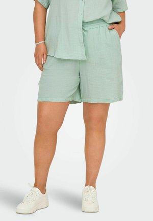 Mint green, lightweight shorts with an elastic waistband, two side pockets, and a textured finish. Paired with white sneakers.