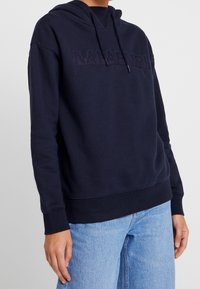 Sudadera azul marino de tejido suave, con un parche de logo en el frente, capucha ajustable con cordón y puños acanalados, con un corte relajado.