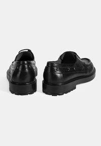 Schwarze Leder Schuhe mit strukturiertem Finish, rundem Zehenbereich und einer dicken, gemusterten Gummisohle. Die Rückansicht zeigt die Schnürdetails.