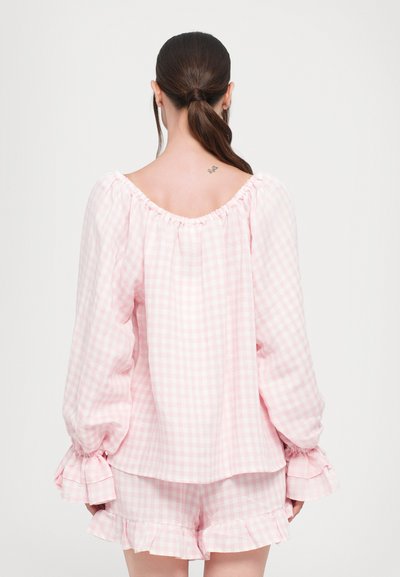 Blouse à carreaux vichy rose avec des manches bouffantes et des poignets volantés, associée à un short assorti, mettant en avant une coupe décontractée et un tissu léger.