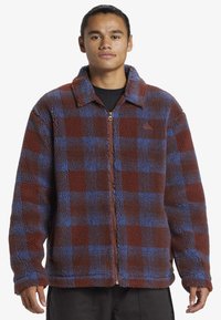 Veste en polaire à motif vichy marron et bleu, dotée d'une fermeture éclair à l'avant, d'un col pointu et d'un tissu texturé pour la chaleur.