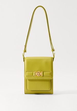 Bolsa de couro verde com um formato estruturado, apresentando uma aba frontal, detalhes em metal dourado e uma alça ajustável e esbelta.