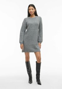 Siva pletena obleka s okroglih izrezom, dolgimi nabranimi rokavi in rahlo razširjenim robom. Oblečena z visokimi črnimi usnjenimi škornji.