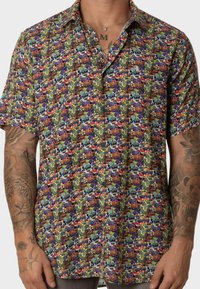 Camisa de manga corta con un colorido patrón gráfico que presenta diversos diseños sobre un fondo azul claro, fabricada con un tejido ligero.