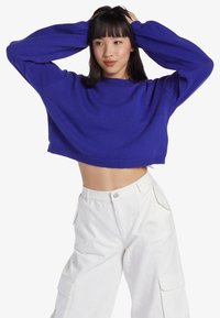 Gekürzter, gestrickter Pullover in Königsblau, mit langen Ärmeln und gerippter Textur, kombiniert mit hochtaillierten weißen Cargo-Hosen.