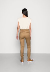 Béžové přiléhavé kalhoty s hladkou texturou, zkombinované s krémovým volně střiženým topem. Obuv zahrnuje hnědé tenisky s bílou podrážkou.